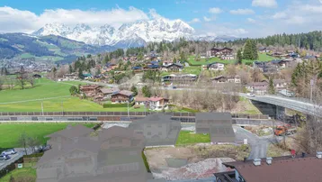 Luftaufnahme einer Wohngegend mit schneebedeckten Bergen im Hintergrund und grünen Feldern.