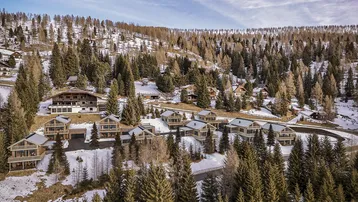 Luftaufnahme einer Gruppe von modernen Chalets in einer verschneiten Berglandschaft.