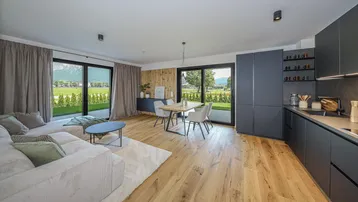 Moderner offener Wohn-Essbereich mit integrierter Küche, Holzboden und Zugang zur Terrasse mit Bergblick.