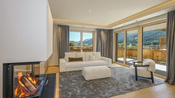 Helles Wohnzimmer mit modernem Kamin, bequemen Sofas und Zugang zu einer Terrasse mit Bergblick.