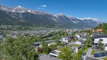 Panoramablick auf die Stadt und die umliegende Berglandschaft unter blauem Himmel.