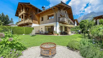 Großzügiger Gartenbereich mit Rasenfläche, Feuerstelle und Blick auf das traditionelle Holzhaus.