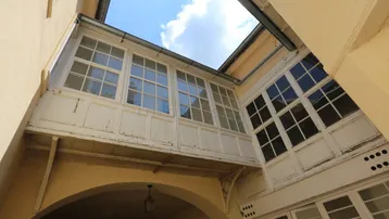 Blick in einen historischen Innenhof mit einem verglasten Wintergarten und einem Torbogen.