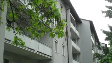 Mehrfamilienhaus mit mehreren Balkonen und gepflegter Grünfläche vor dem Gebäude.