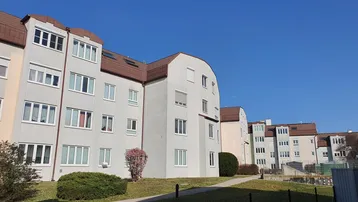 Mehrere Wohngebäude mit heller Fassade und begrünten Außenanlagen unter blauem Himmel.