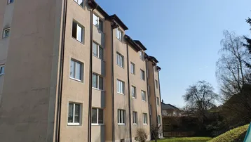 Mehrfamilienhaus mit beigefarbener Fassade und gepflegter Rasenfläche unter blauem Himmel.