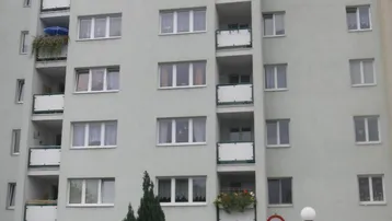 Mehrstöckiges Wohngebäude mit zahlreichen Balkonen und einer kleinen Grünfläche im Vordergrund.