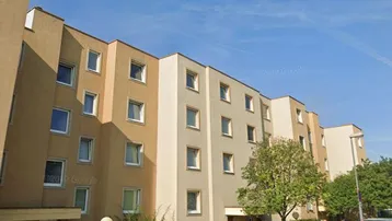 Mehrstöckiges Wohngebäude mit beiger Fassade, vielen Fenstern und Parkplätzen im Freien.