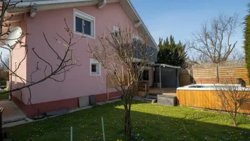 Ansicht des Hauses von der Seite mit Garten, Rasenfläche und integriertem Whirlpool auf einem Holzdeck.