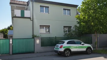 Vorderansicht des Hauses mit hellgrüner Fassade, Fenstern und einem gepflegten Vorgartenbereich.
