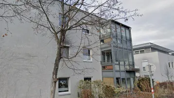 Modernes Mehrfamilienhaus mit grauer Fassade und verglastem Treppenhaus oder Balkonstruktur.