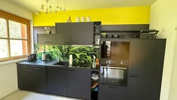 Moderne schwarze Einbauküche mit grüner Rückwand und gelber Akzentwand im Dachgeschoss.