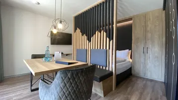 Moderner Wohn- und Essbereich mit Holzboden und integriertem Schlafbereich, abgetrennt durch eine stilvolle Lamellenwand.