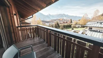 Geräumiger Holzbalkon mit Sitzgelegenheiten und weitem Blick auf die umliegende Berglandschaft.