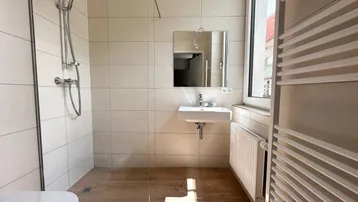 Modernes Badezimmer mit ebenerdiger Dusche, Wand-WC, Waschbecken und beheiztem Handtuchhalter.