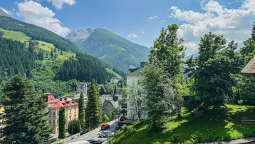 Malerischer Blick auf eine Bergstadt mit grünen Hängen und traditionellen Gebäuden unter blauem Himmel.