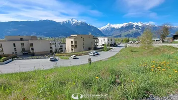 Panoramablick auf moderne Wohngebäude mit schneebedeckten Bergen im Hintergrund unter blauem Himmel.
