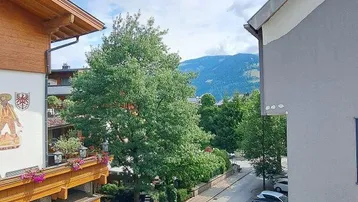 Blick vom Balkon auf die Straße, umliegende Gebäude und die dahinterliegende Berglandschaft unter blauem Himmel.