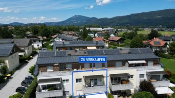 Luftaufnahme eines modernen Wohnkomplexes mit Balkonen und Bergblick, eine Einheit ist zum Verkauf markiert.