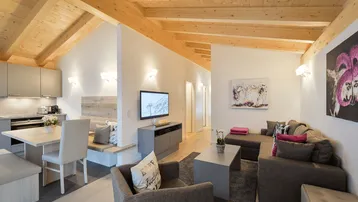 Offener Wohnbereich mit integrierter Küche, Essbereich und Holzbalkendecke im modernen alpinen Stil.