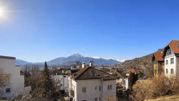 Weitläufiger Panoramablick über eine Stadtlandschaft mit schneebedeckten Bergen im Hintergrund.
