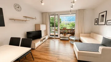 Helles Wohn- und Esszimmer mit Holzboden, Balkonzugang und weitem Bergblick.