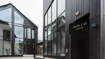 Moderne Gebäude mit dunkler Holzfassade und großen Glasfronten, die Eingänge zu den Studios zeigen.