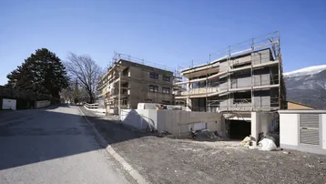 Neubauwohnungen im Bau mit Gerüst und Blick auf die umliegende Berglandschaft.