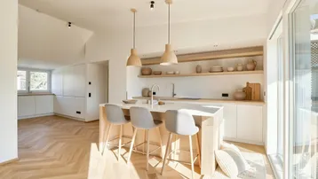 Helle, moderne Küche mit Kochinsel, Holzboden und Zugang zu einem sonnigen Balkon.