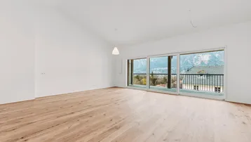 Helles, leeres Zimmer mit Holzboden und großen Fenstern, die einen weiten Bergblick bieten.