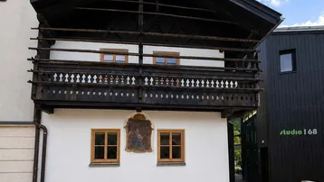 Traditionelles Gebäude mit Holzbalkon und weißer Fassade unter blauem Himmel.