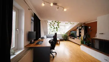 Geräumiges Wohnzimmer im Dachgeschoss mit Arbeitsbereich, Holzboden und Blick ins Grüne.