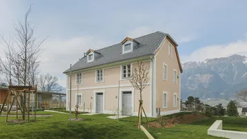 Elegantes Wohnhaus mit heller Fassade, umgeben von Grünflächen und Bergblick.