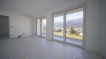 Heller, unmöblierter Wohnraum im Rohbau mit großen Fenstern und Bergblick.