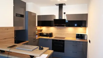 Moderne Küche mit grauen Hochglanzfronten, Holzarbeitsplatten und integrierten Geräten für effizientes Kochen.