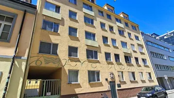 Gelbes Mehrfamilienhaus mit mehreren Etagen und Dachgauben unter blauem Himmel.