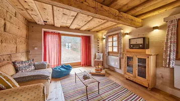 Gemütliches Wohnzimmer im alpinen Stil mit Holzbalkendecke, Holzboden und großem Fenster zum Garten.
