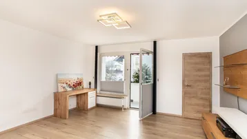 Geräumiges Wohnzimmer mit Holzboden, Schreibtischbereich und Zugang zum Außenbereich.
