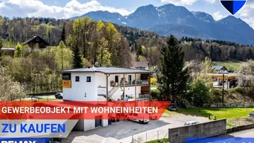 Großes Gewerbeobjekt mit Wohnungen in den oberen Etagen, umgeben von Bergen und grüner Landschaft.
