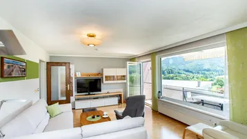 Helles Wohnzimmer mit großem Fenster, Holzboden und Panoramablick auf die umliegende Natur.