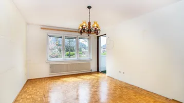 Helles Zimmer mit Fischgrätparkett, großem Fenster und Blick ins Grüne, ausgestattet mit einem klassischen Kronleuchter.