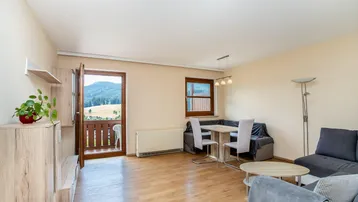 Helles Wohn- und Esszimmer mit Holzboden, gemütlicher Sitzecke und Zugang zum Balkon mit Bergblick.