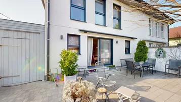 Geräumige gepflasterte Terrasse hinter dem Haus mit Gartenmöbeln und Zugang zum Innenbereich.
