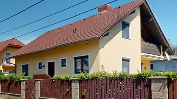 Charmantes Einfamilienhaus mit gelber Fassade, rotem Ziegeldach und Balkon.