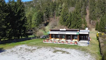 Freistehendes Restaurant mit Außenbereich und weitläufiger Schotterfläche, umgeben von Wald.