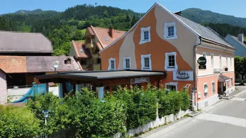 Traditionelles Gebäude mit markanter orangefarbener Fassade und grüner Bepflanzung, umgeben von Bergen.