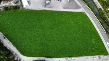 Senkrechte Luftaufnahme eines großen, rechteckigen grünen Grundstücks neben einer Straße und einem Fluss.