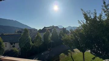 Sonniger Balkon mit weitem Blick auf die umliegende Berglandschaft und grüne Umgebung.