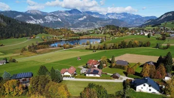Panoramablick auf eine ländliche Landschaft mit See, Bergen und verstreuten Wohnhäusern.