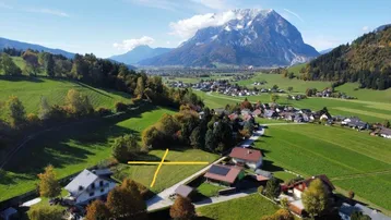 Luftaufnahme einer ländlichen Gegend mit Häusern, grünen Wiesen und einem majestätischen Berg im Hintergrund.